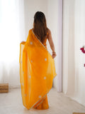 Woman wearing a bright yellow saree with white patterns in a minimal indoor setting Glanzavi.