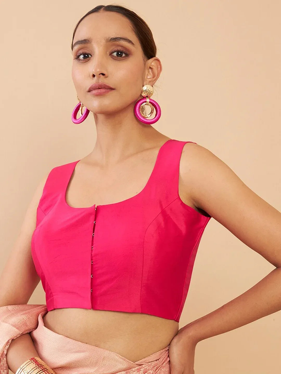 Woman wearing a bright pink top with large hoop earrings on a beige background Glanzavi