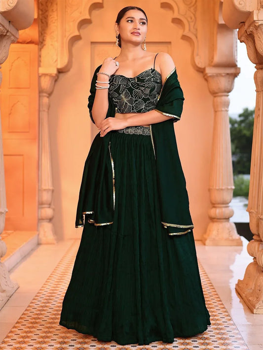 Woman in a dark green traditional outfit with floral patterns standing in front of ornate architectural elements Glanzavi.