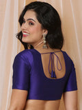 Woman wearing a purple blouse with a cut-out back design against a beige curtain Glanzavi.