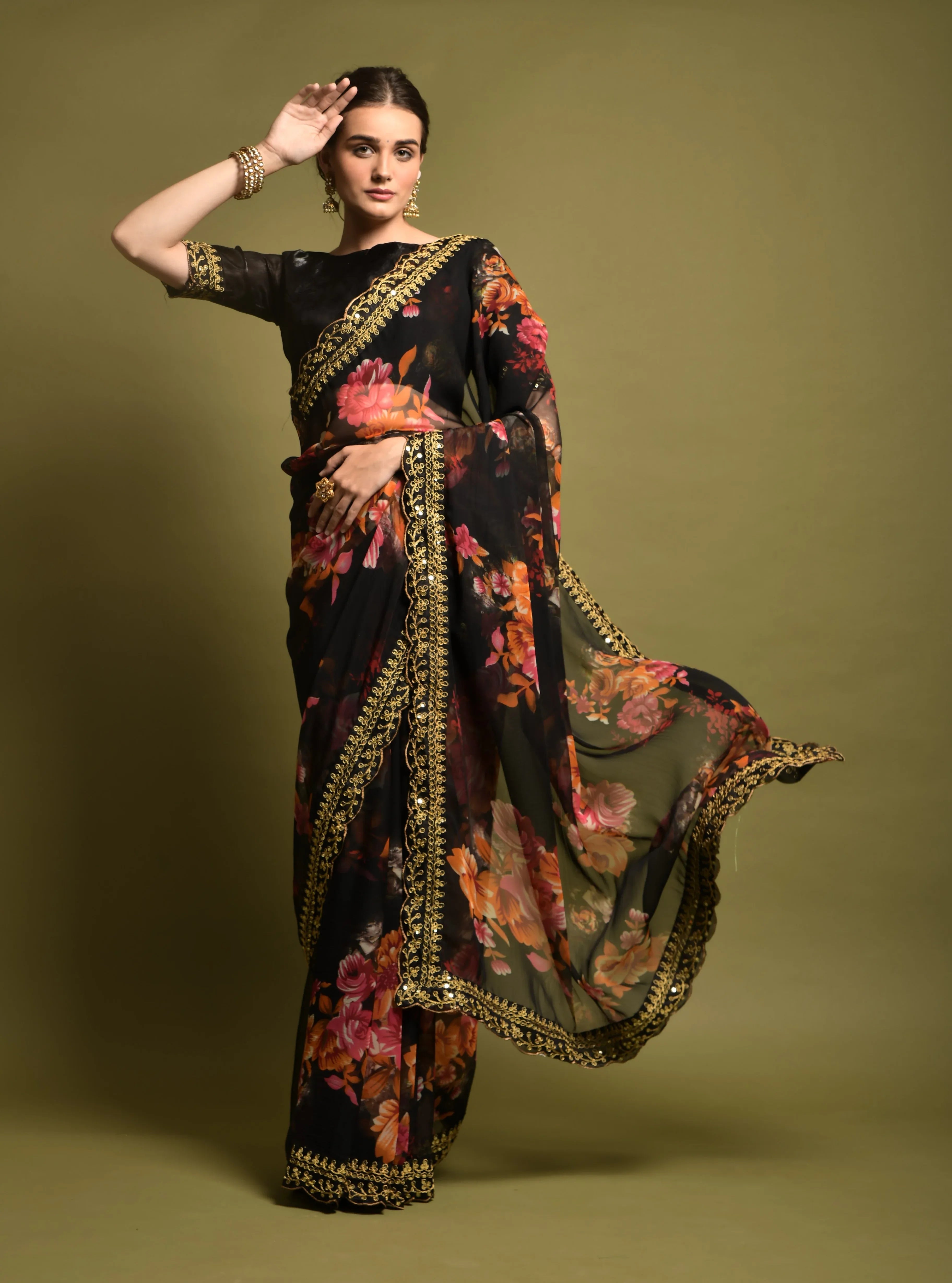 Woman wearing a black floral saree with a gold border on a green background Glanzavi