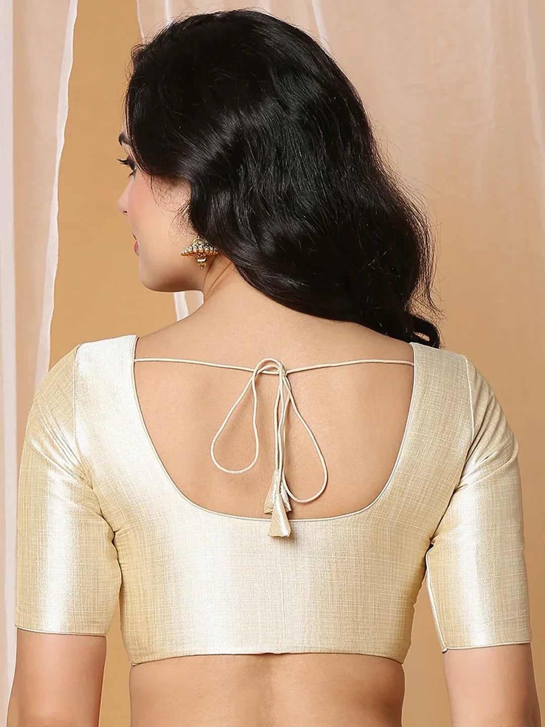 Woman wearing a cream blouse with a unique back design against a beige background Glanzavi