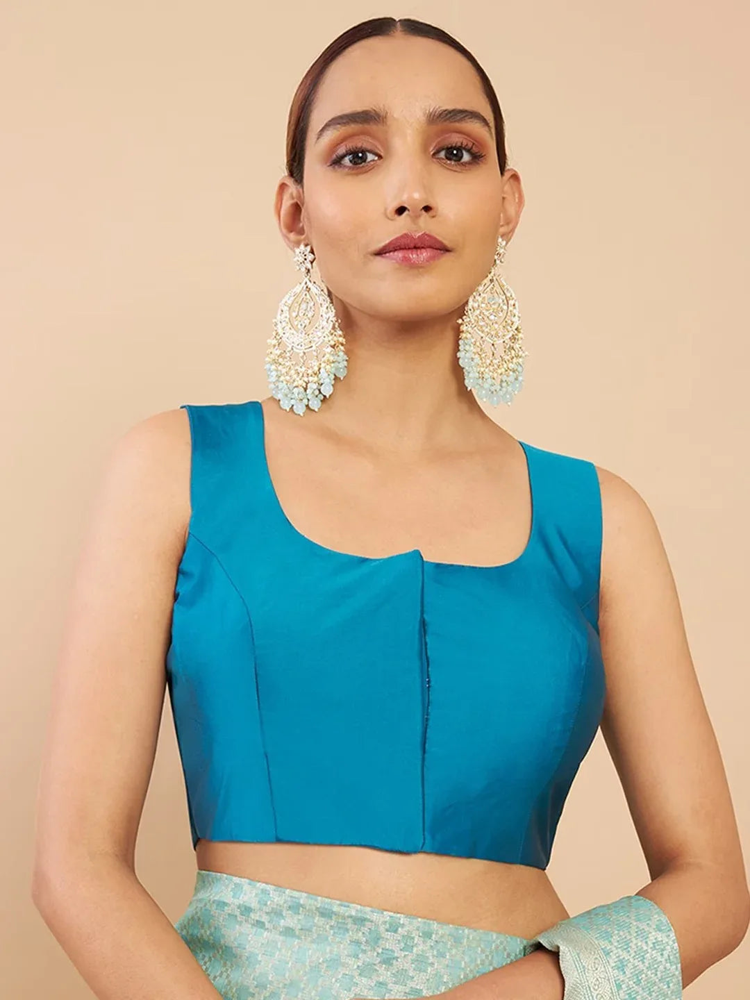 Woman wearing a blue top and green skirt with large earrings on a beige background Glanzavi