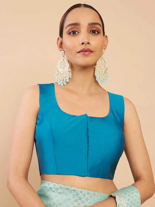Woman wearing a blue top and green skirt with large earrings on a beige background Glanzavi