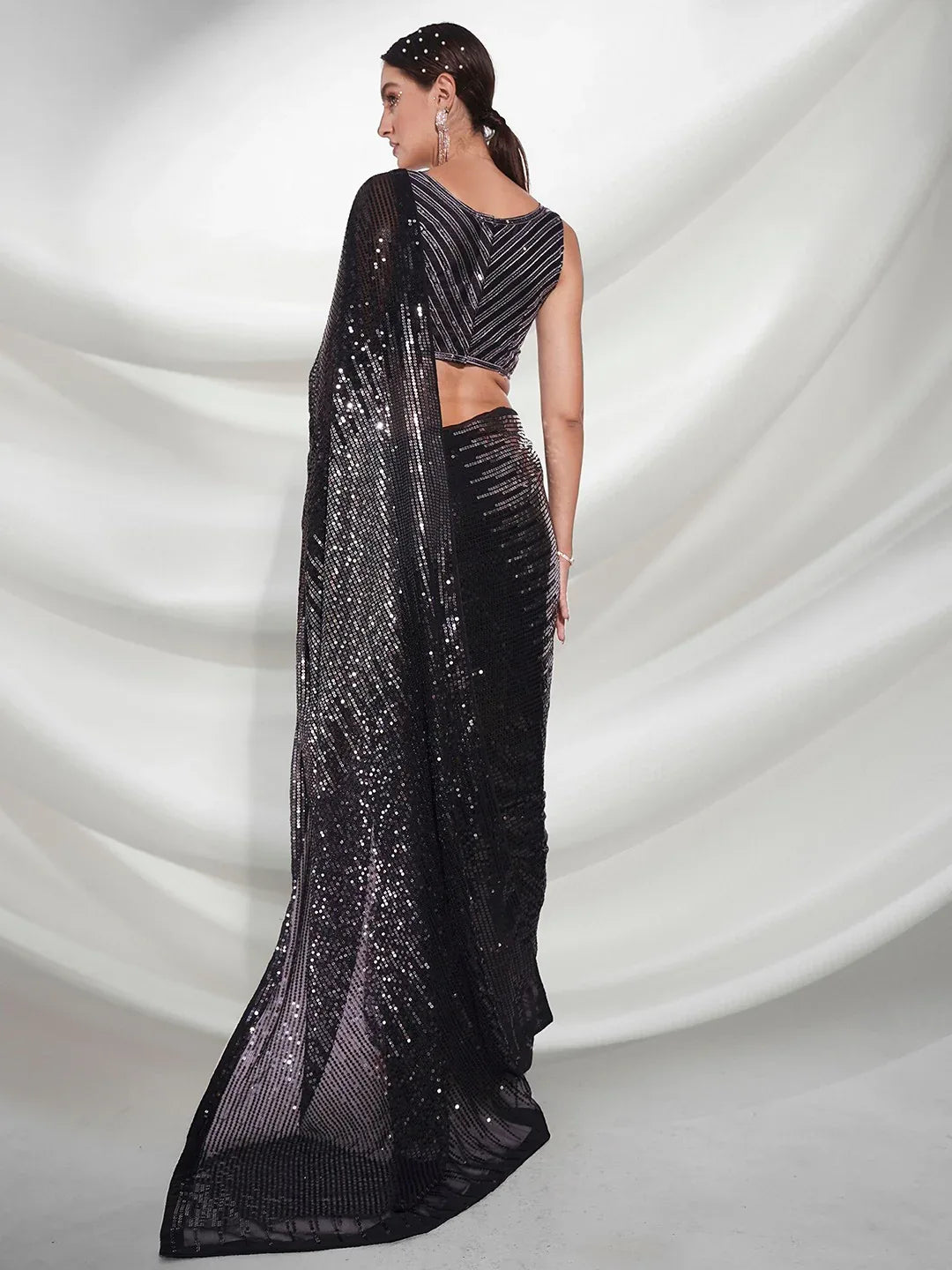 Black saree with sequins on a white draped fabric background Glanzavi