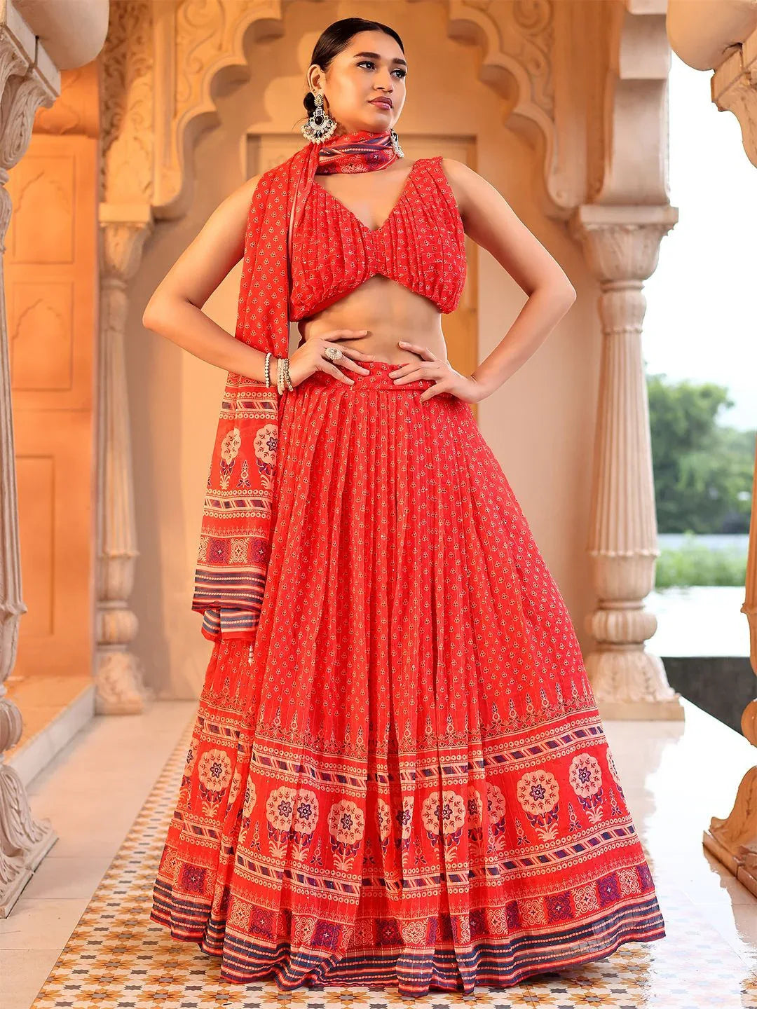 Woman in a red traditional outfit with patterns standing in an ornate architectural setting Glanzavi.