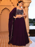Woman in a dark purple saree with a black blouse standing in front of an architectural background Glanzavi.