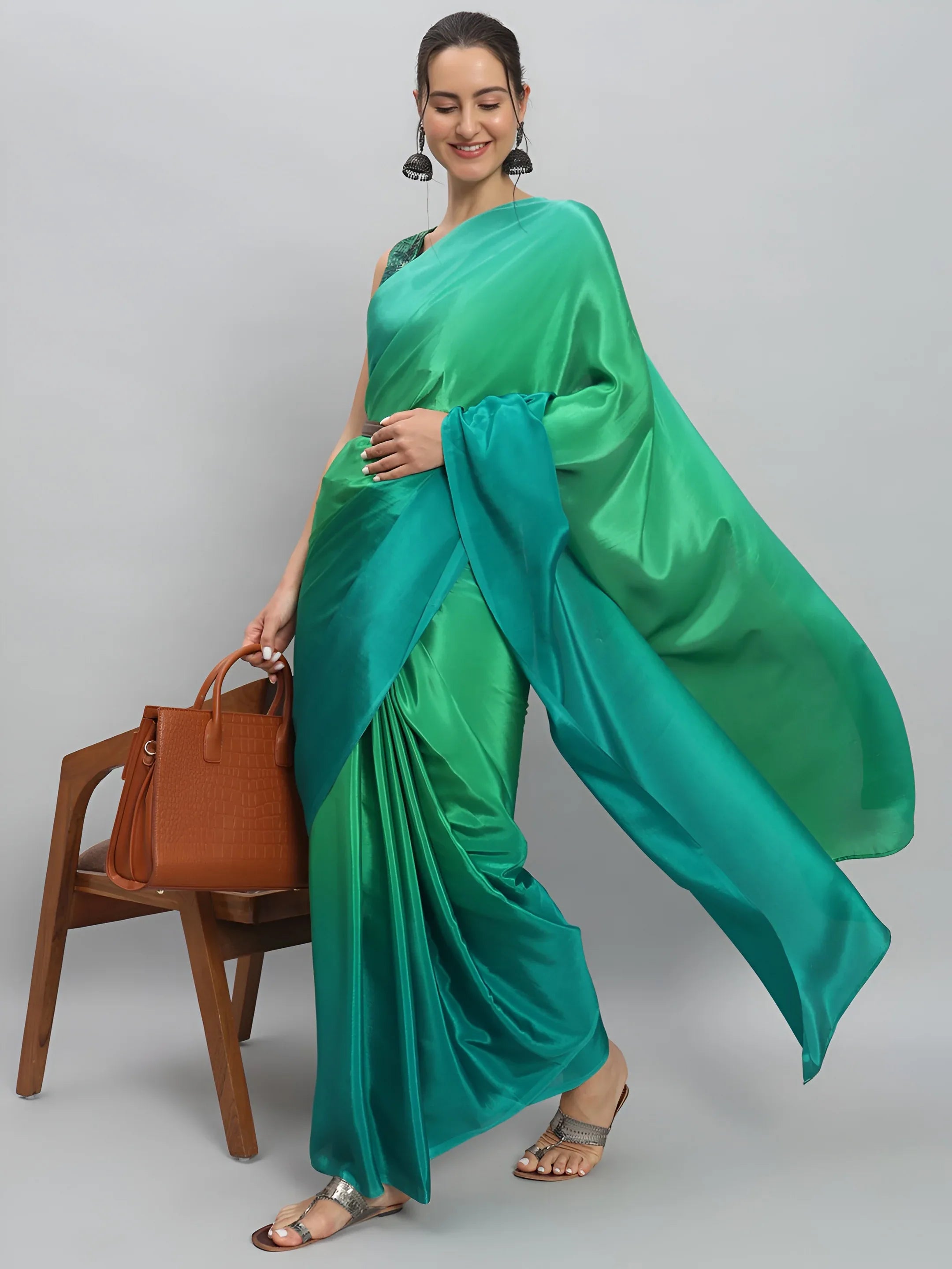 Woman wearing a green saree holding a brown handbag against a gray background Glanzavi