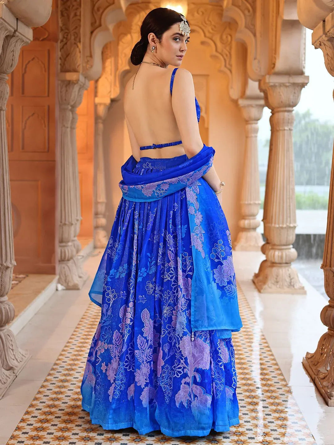 Woman in a blue embroidered traditional outfit standing in an ornate architectural setting Glanzavi.