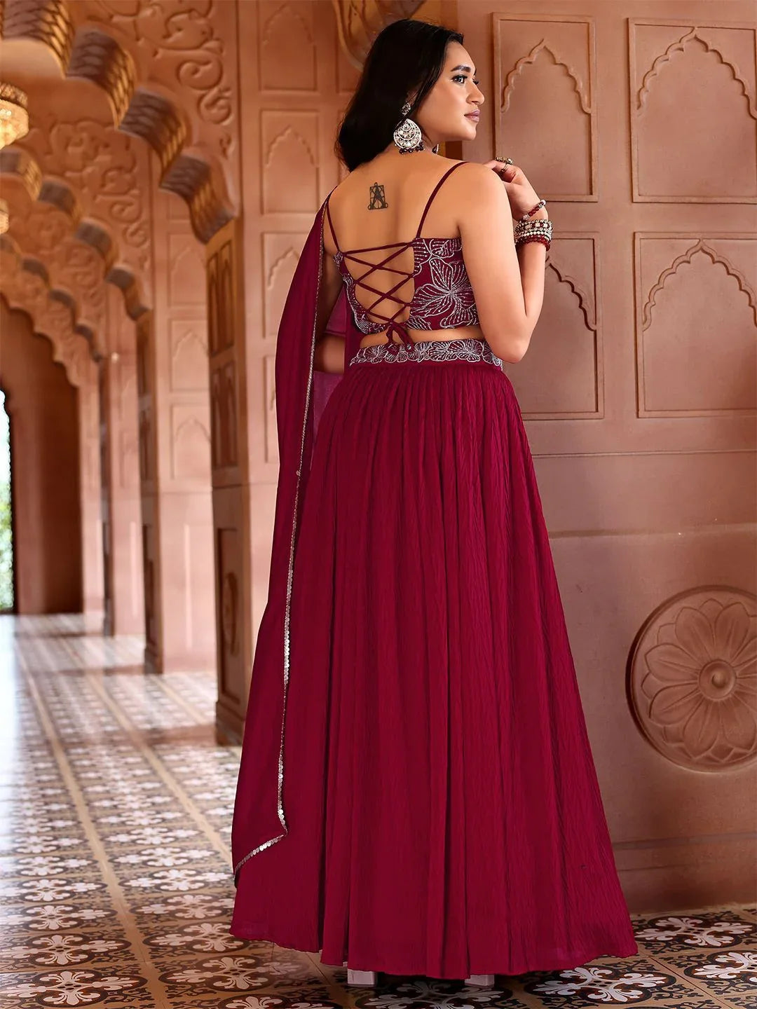 Woman in a burgundy evening gown with intricate back design standing in front of an ornate wall Glanzavi.