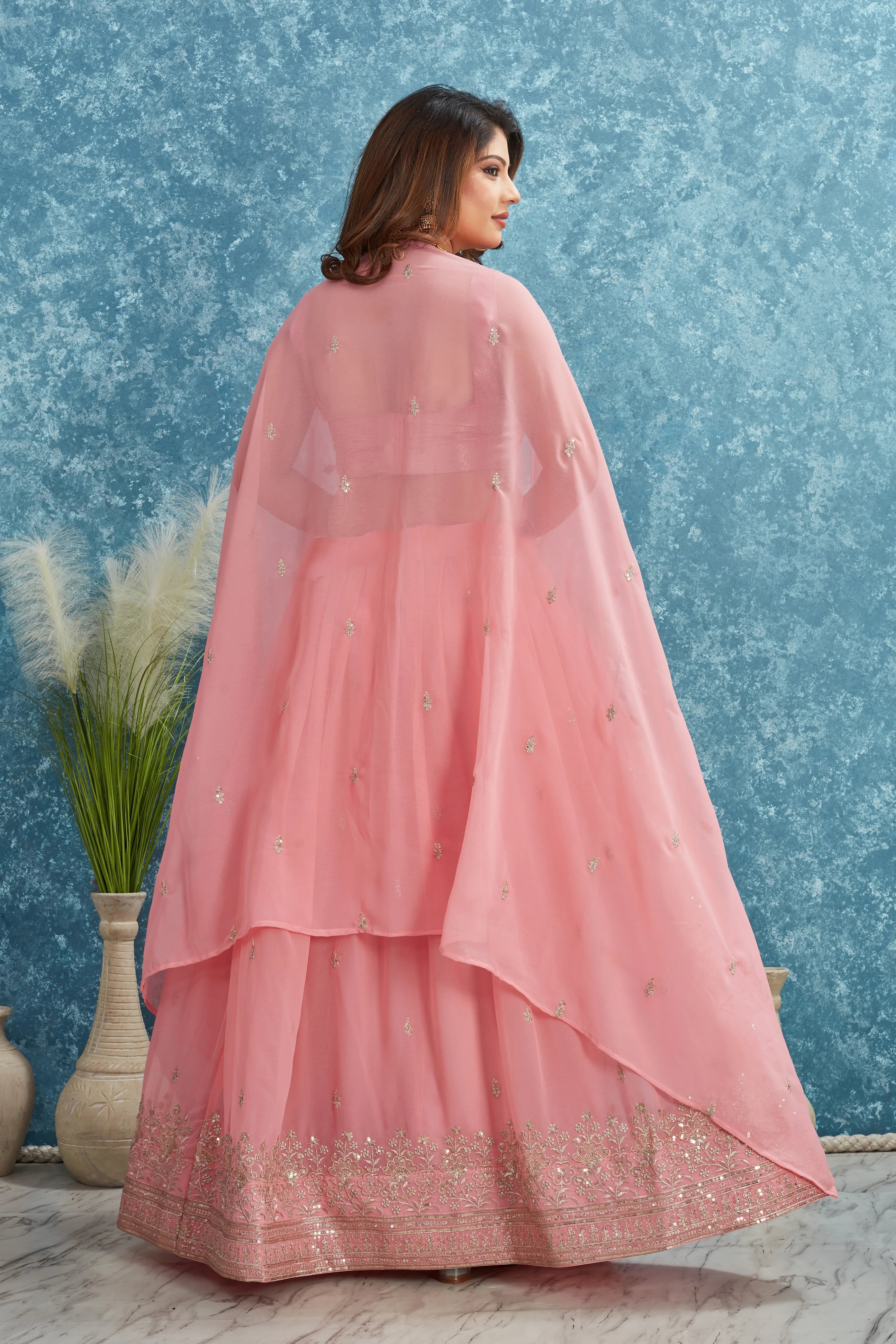 Woman wearing a pink traditional outfit with a blue textured wall background Glanzavi