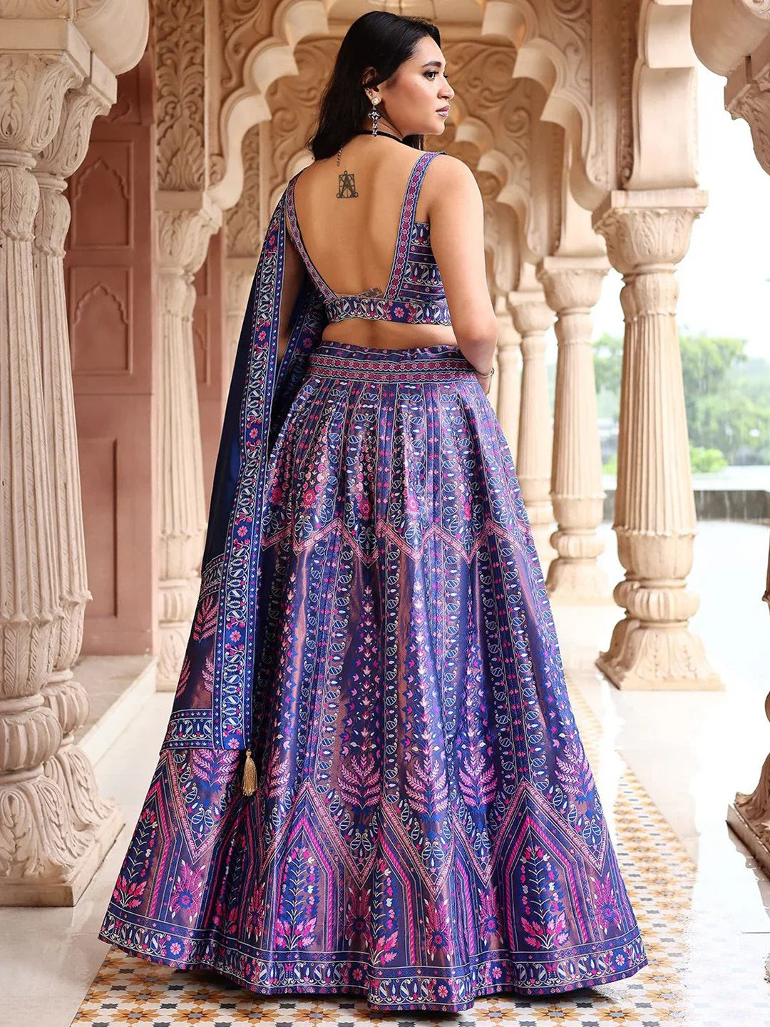 Woman wearing a purple patterned saree with a traditional architectural background Glanzavi