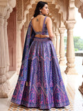 Woman wearing a purple patterned saree with a traditional architectural background Glanzavi