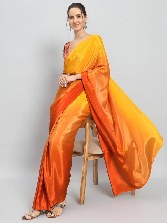 Woman wearing an orange and yellow saree sitting on a chair against a gray background Glanzavi