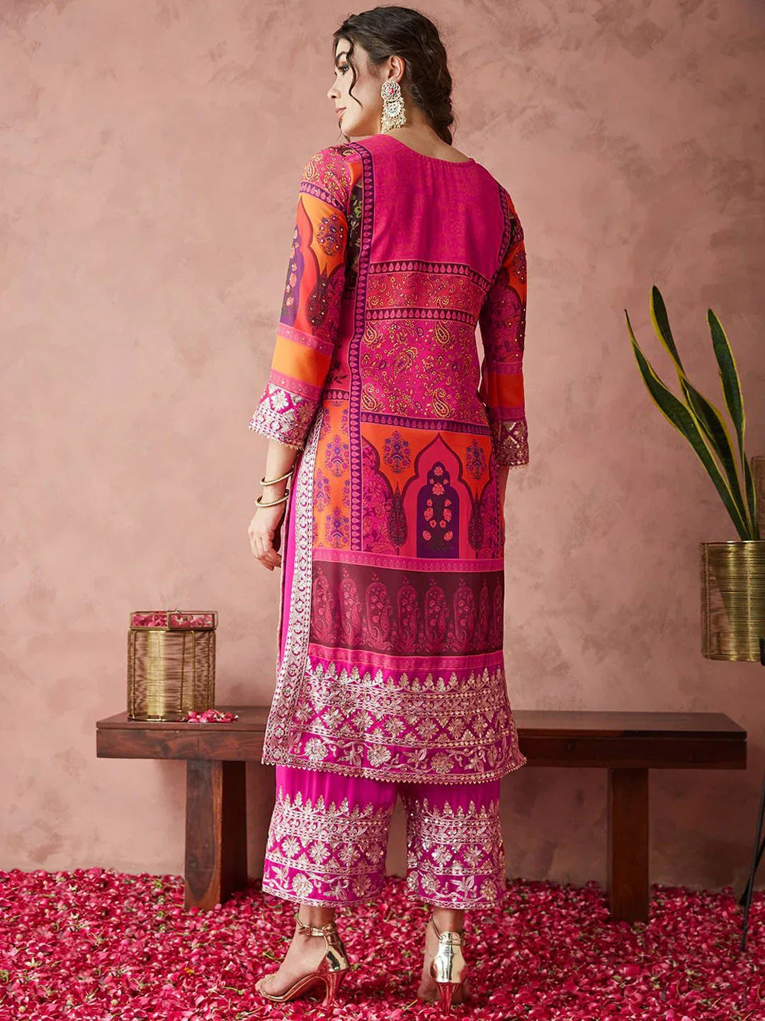 Woman wearing a pink traditional outfit with intricate patterns, standing on red flowers against a pink background Glanzavi