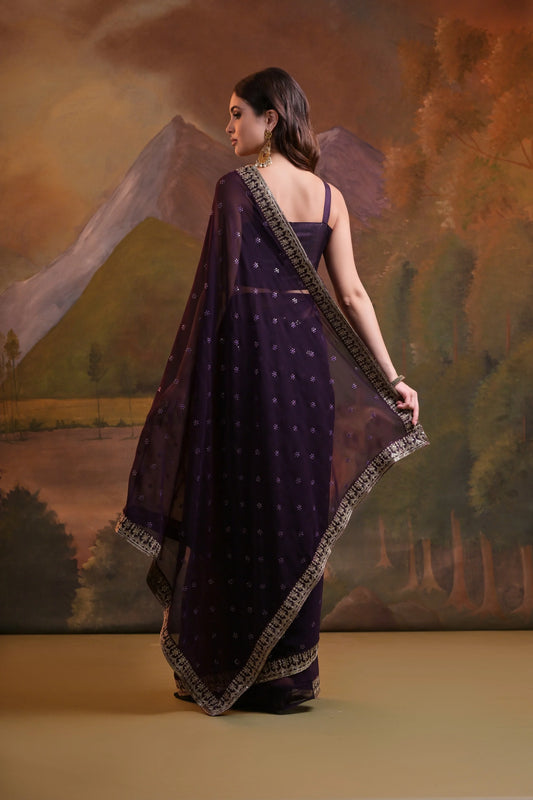 Woman in a dark purple saree with gold border against a scenic backdrop Glanzavi