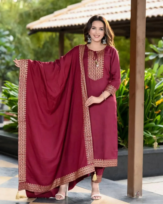 Woman in a maroon traditional outfit with gold embroidery standing outdoors Glanzavi