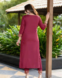 Woman in a maroon kurta with gold embroidery standing outdoors near greenery Glanzavi