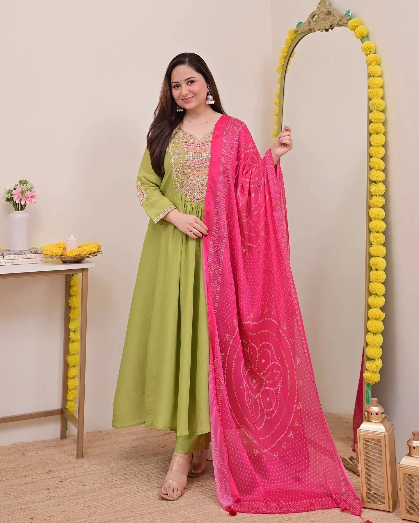 Woman in green outfit with pink dupatta standing next to a decorative mirror Glanzavi