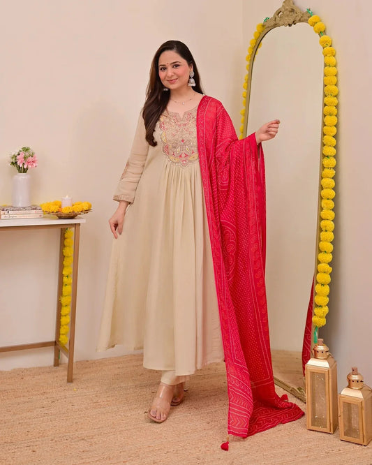 Woman in a beige anarkali suit with a red dupatta standing next to a decorative mirror Glanzavi