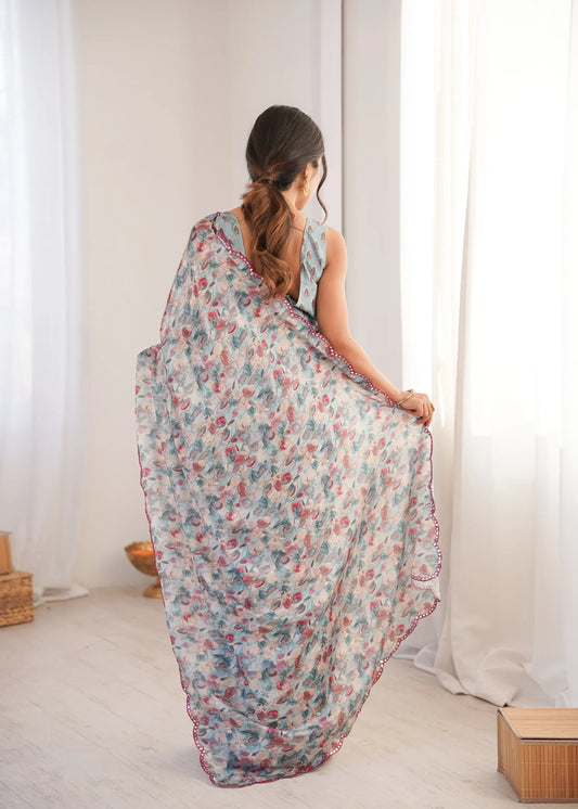 Woman in a floral saree standing in a room with white curtains Glanzavi.