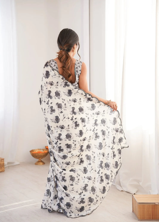 Woman wearing a floral dress sitting on a white floor with a white curtain in the background Glanzavi