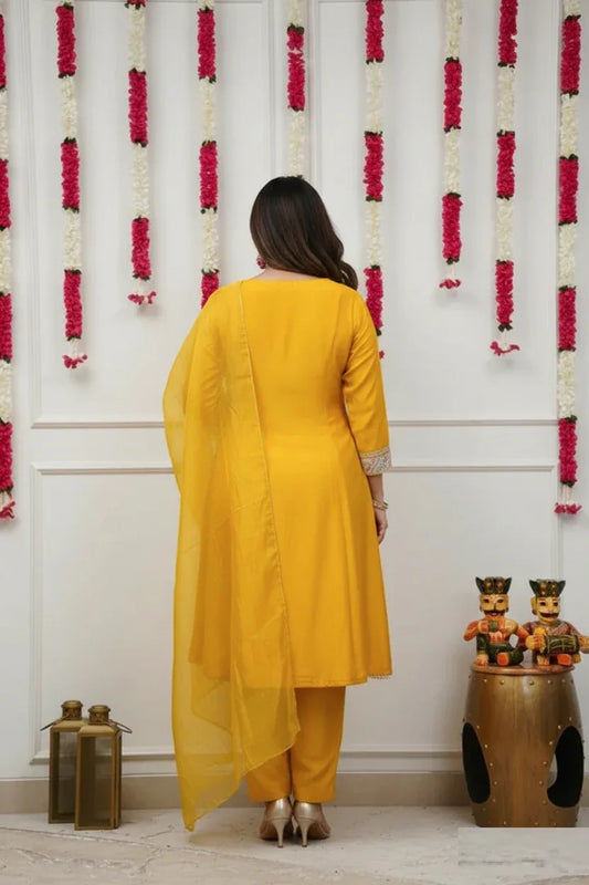 Woman in a yellow traditional outfit standing in front of a decorative wall with floral arrangements Glanzavi