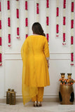 Woman in a yellow traditional outfit standing in front of a decorative wall with floral arrangements Glanzavi