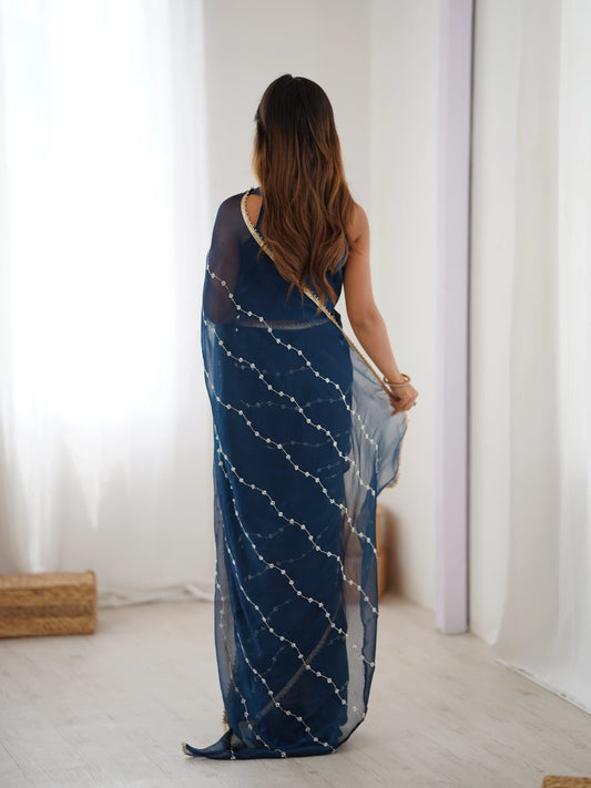 Woman wearing a blue saree with white patterns in a minimalistic room Glanzavi.