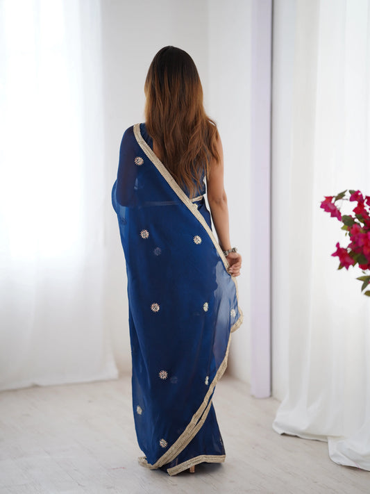 Woman wearing a blue saree with white patterns in a minimalistic setting Glanzavi