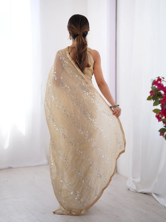 Woman wearing a beige saree with a floral arrangement in the background Glanzavi