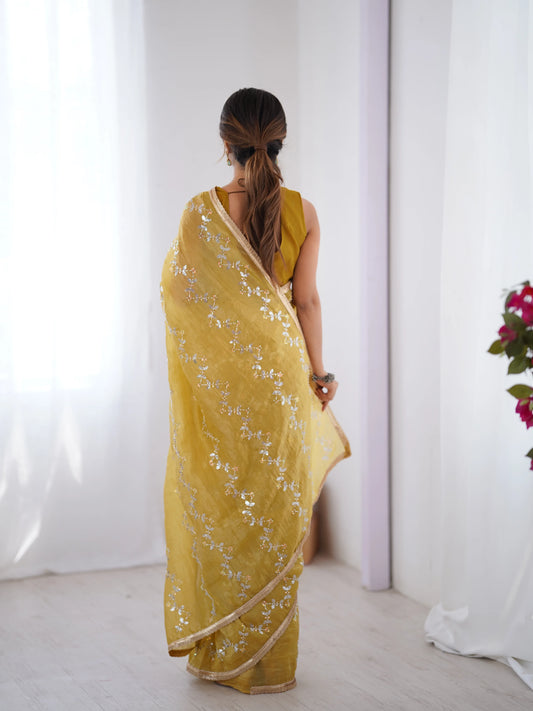 Woman wearing a yellow saree with white floral patterns against a white background Glanzavi