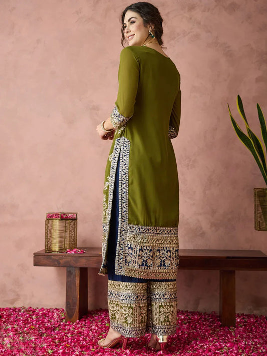 Woman wearing a green and patterned outfit standing in a room with pink walls and rose petals on the floor Glanzavi