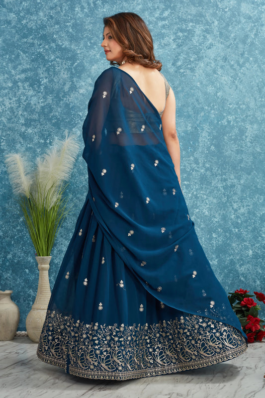 Woman wearing a blue saree with silver embroidery against a textured blue wall Glanzavi.