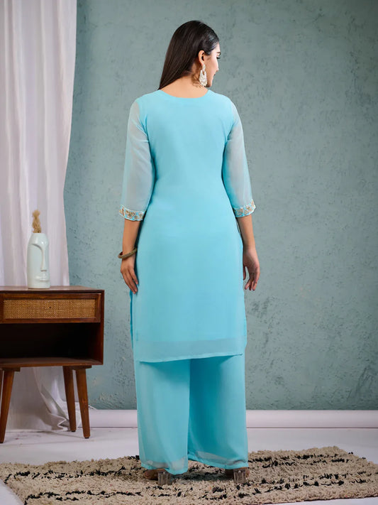 Woman wearing a light blue traditional outfit in a room with a gray wall and wooden furniture Glanzavi