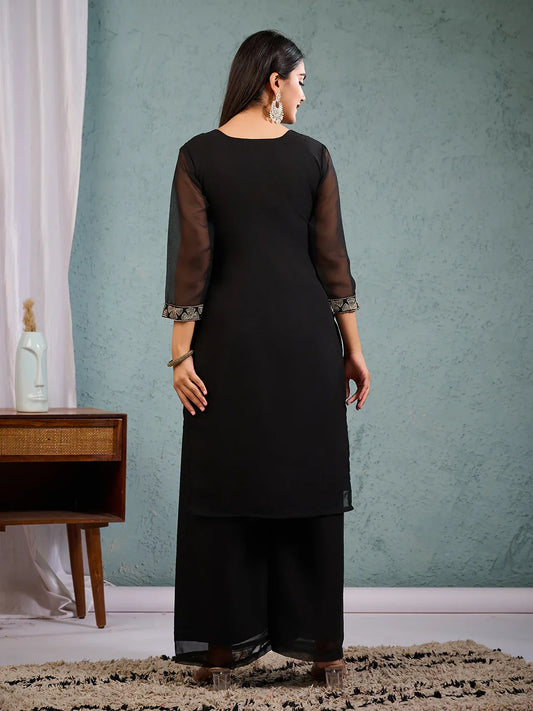 Woman wearing a black kurta with sheer sleeves against a teal wall Glanzavi