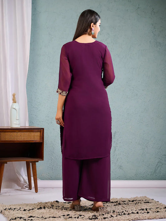 Woman wearing a purple outfit standing in a room with a light blue wall and wooden cabinet Glanzavi