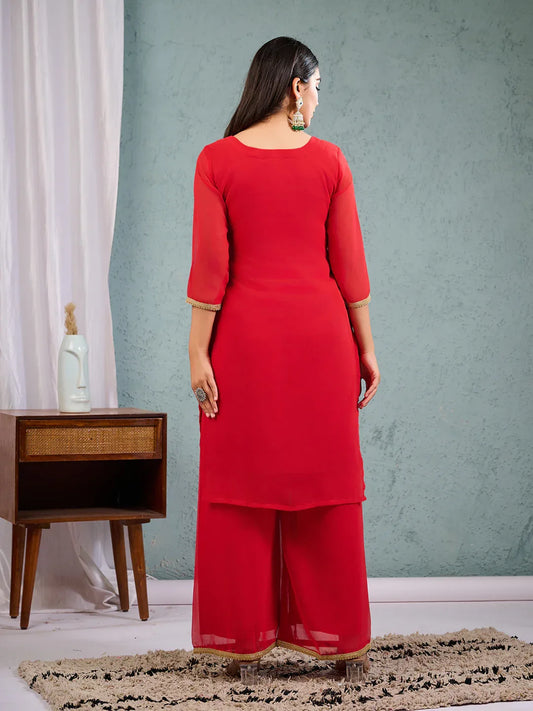 Person wearing a red outfit in a room with a green wall and a wooden side table Glanzavi