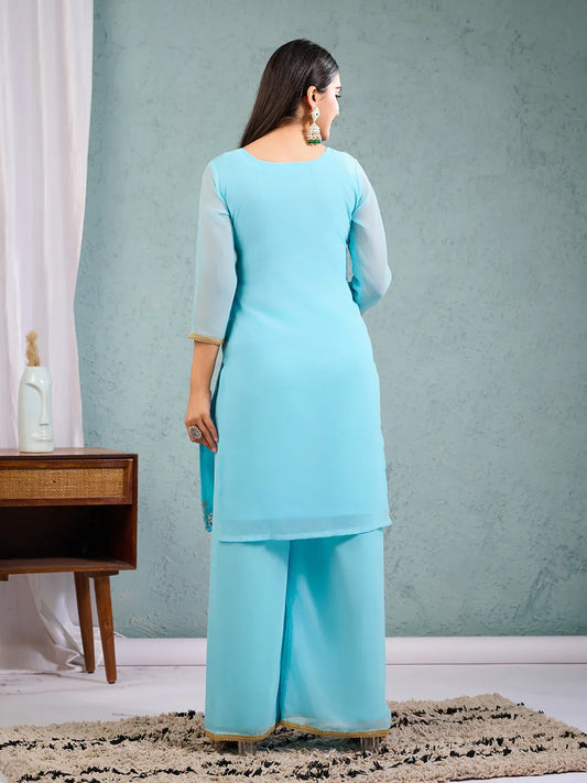 Woman in a blue outfit standing in a room with a blue wall and a wooden desk Glanzavi