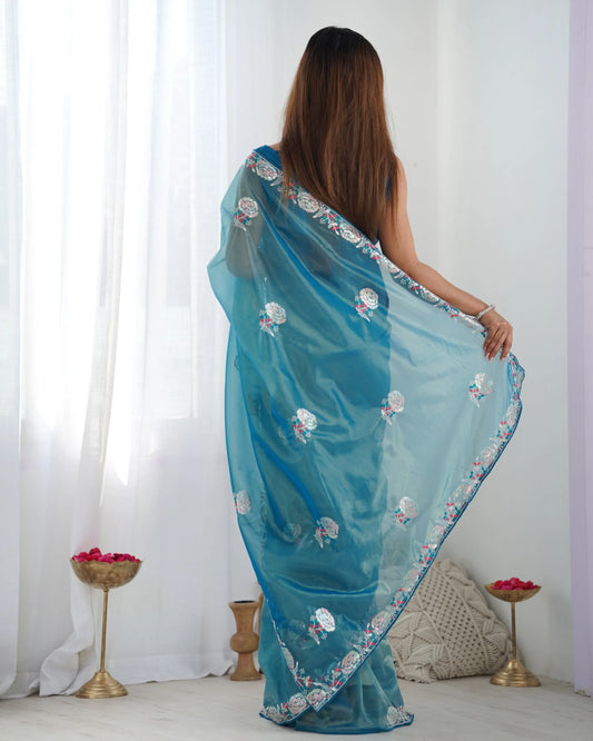 Woman wearing a blue saree with floral patterns in a minimalistic setting Glanzavi