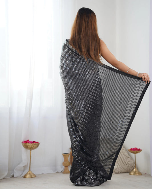 Woman holding a black and silver patterned fabric in a room with white curtains and a basket Glanzavi