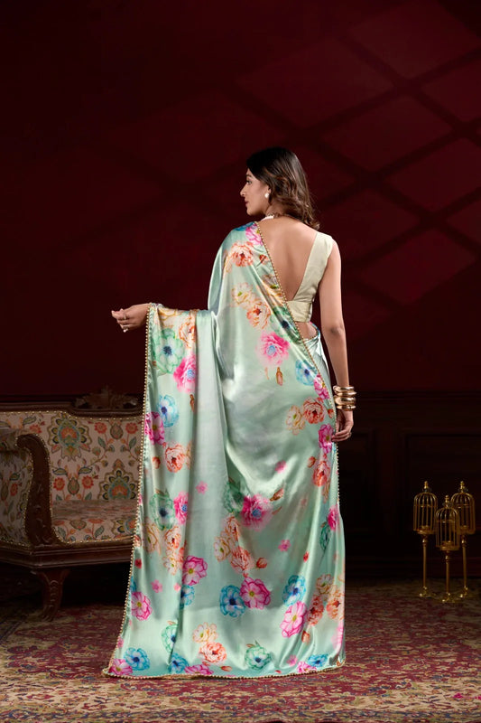 Woman wearing a light green saree with floral patterns in a dimly lit room Glanzavi.