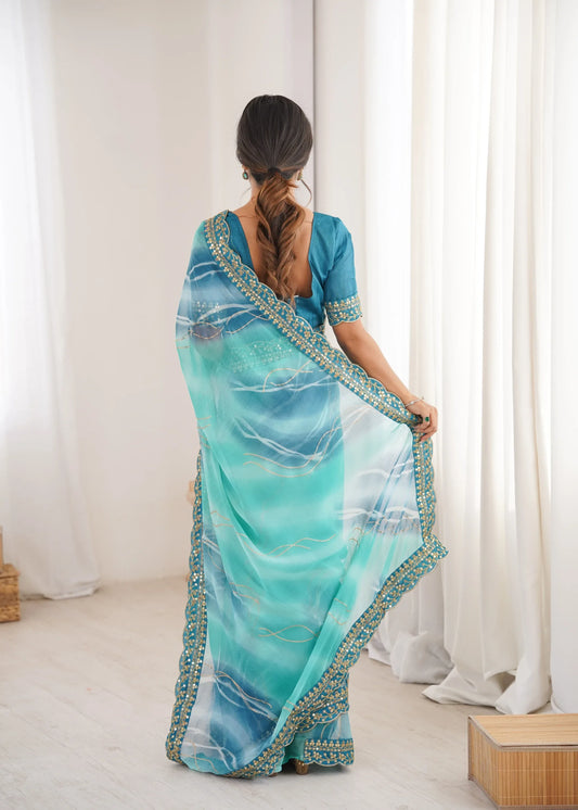 Woman wearing a blue and green saree with a white curtain background Glanzavi